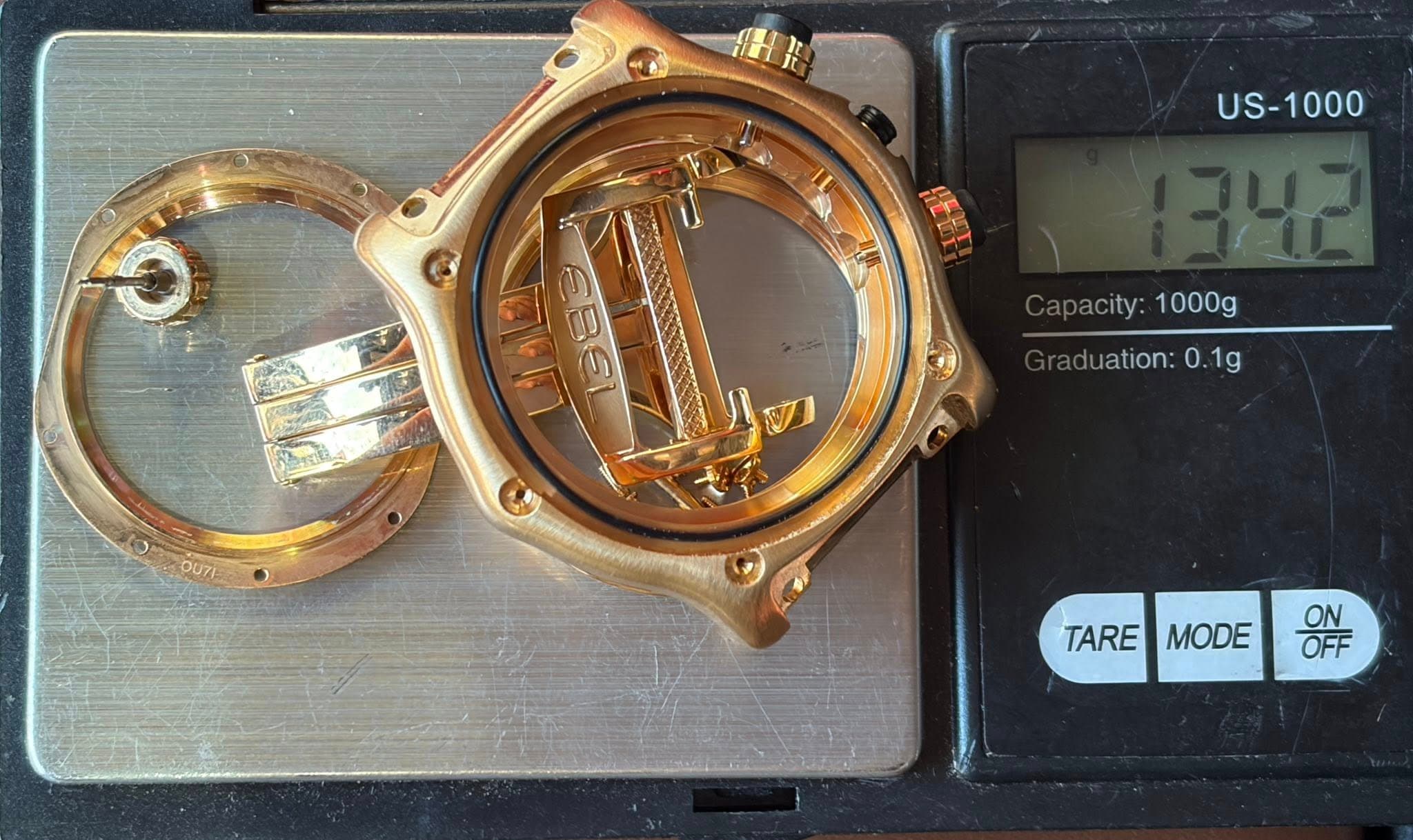 May be an image of wrist watch and text that says 'US-1000 COS EBEL bacity: acity:1000g 1000g luation: aduation:0.1g 0 0.1g TARE MODE ON OFF'