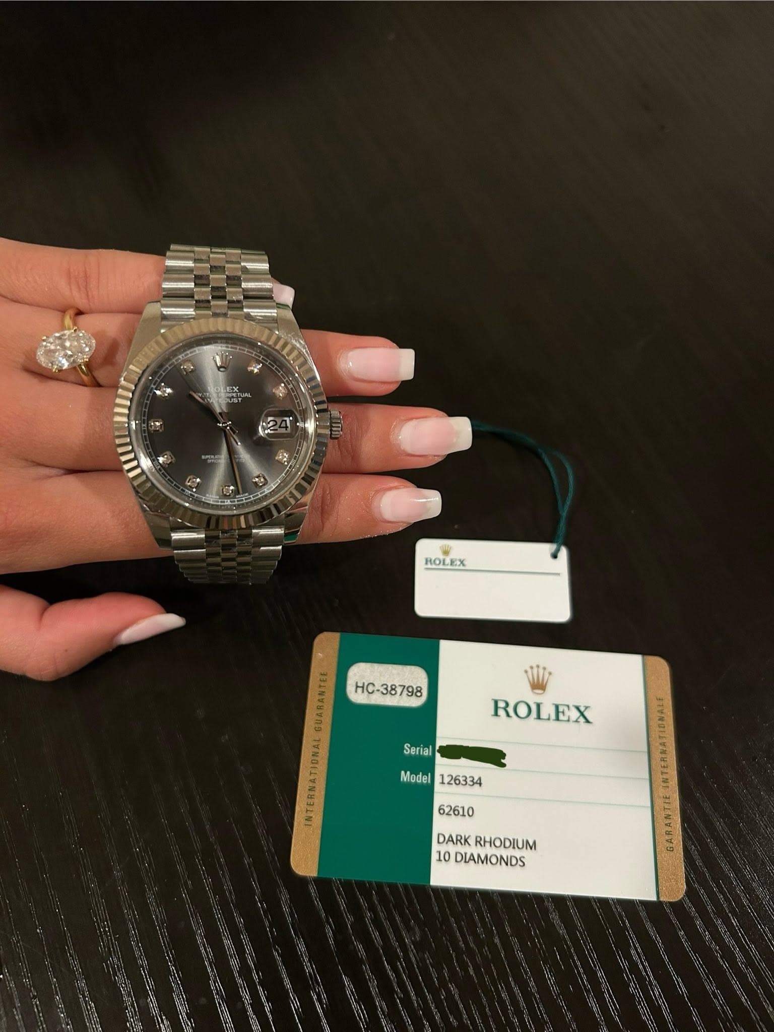 May be an image of money, wrist watch and text that says 'ROLEX QUARANTIE HC-38798 INTERNATIONAL Serial ROLEX Model Model126334 DARK RHODIUM 10 DIAMONDS'