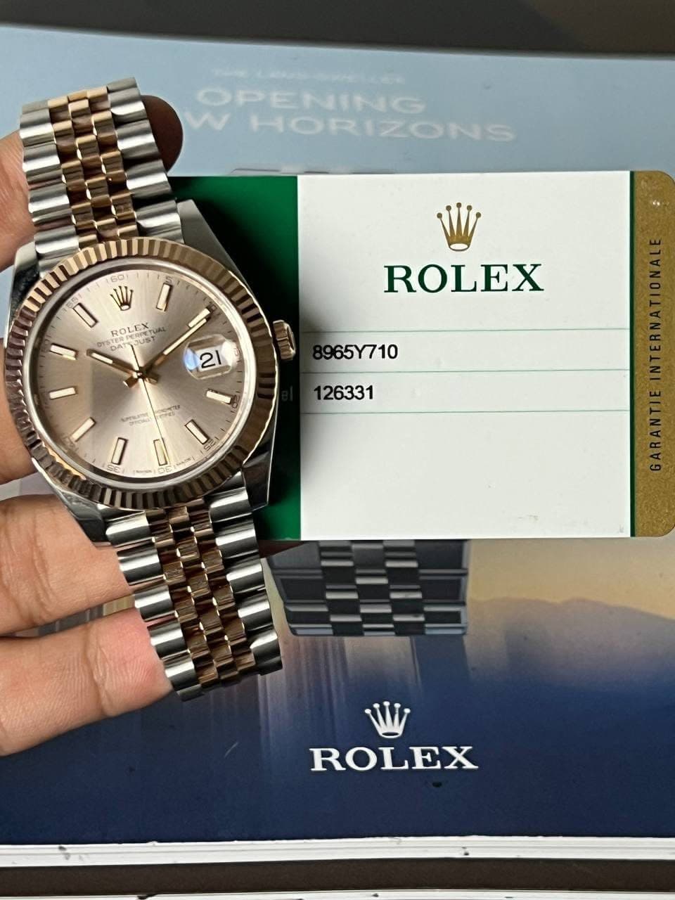 May be an image of wrist watch and text that says 'OPENING WHORIZONS 60 I ROLE ROLEX EREUS ST M OMAT ROLEX 21 965Y710 26331 Pai I 0 I ROLEX'