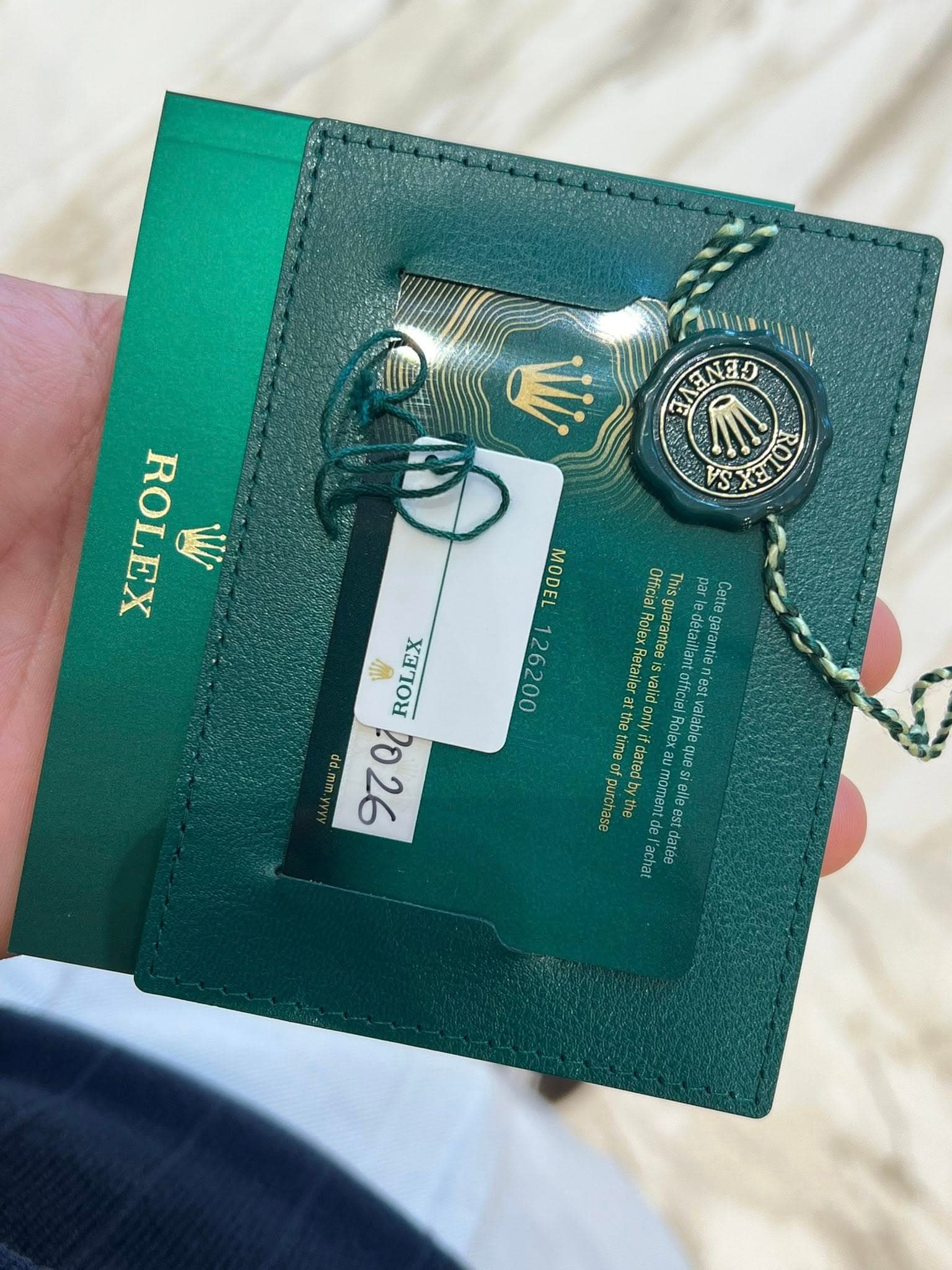 May be an image of money, leather wallet and text that says 'N NAク 网 RO ROLEX W MODEL 126200 Officia 0Hnialal T par/ e celt Cetta RolexRetailer Svalid ofe D'est darantee…
